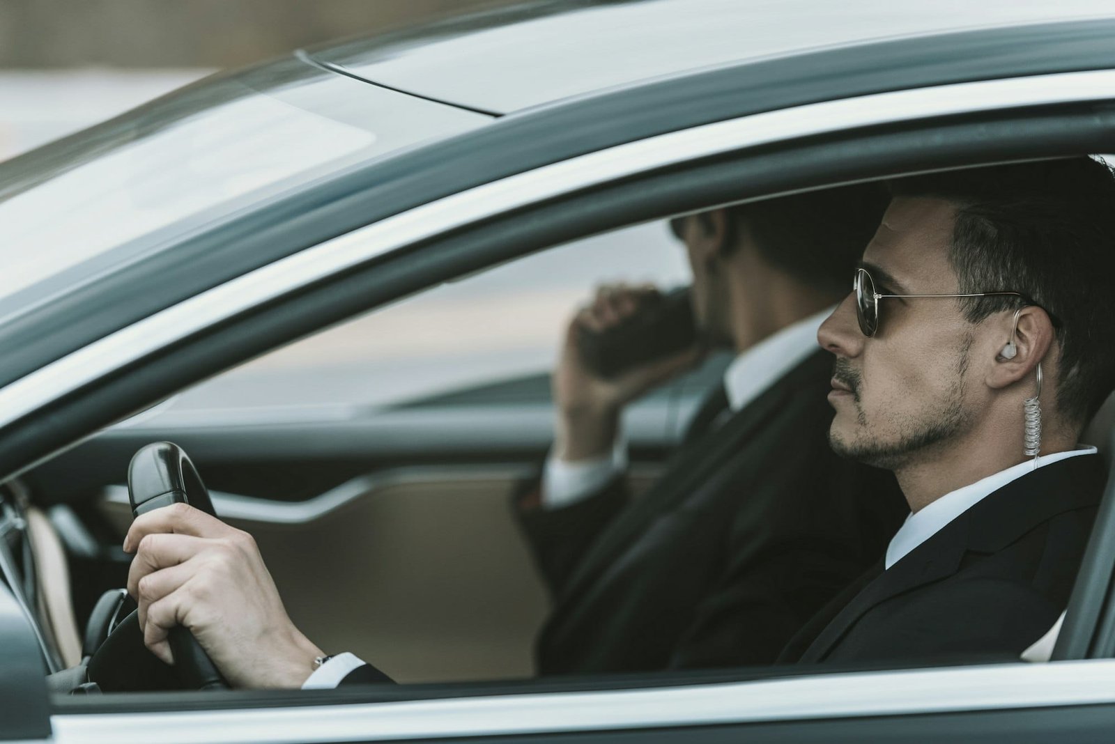 bodyguards with portable radio and security earpiece sitting in a car