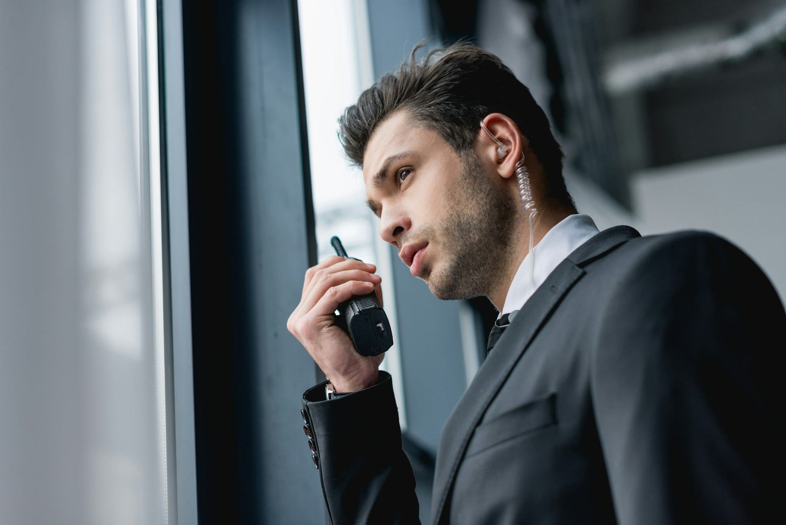 handsome bodyguard with earphone in black suit using walkie-talkie